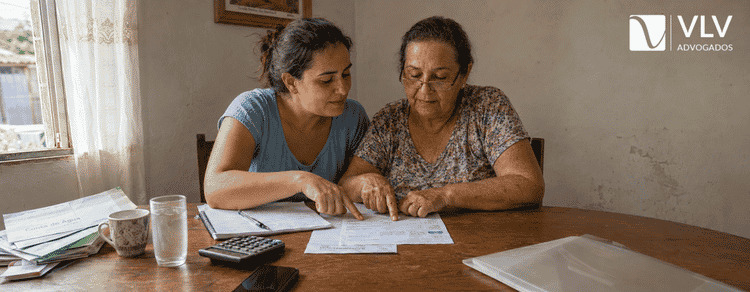 Bolsa Família entra no cálculo do BPC LOAS? Veja a regra! 2 Mulher e mãe idosa conferindo documentos e calculadora sobre a mesa para analisar a renda familiar do BPC LOAS.