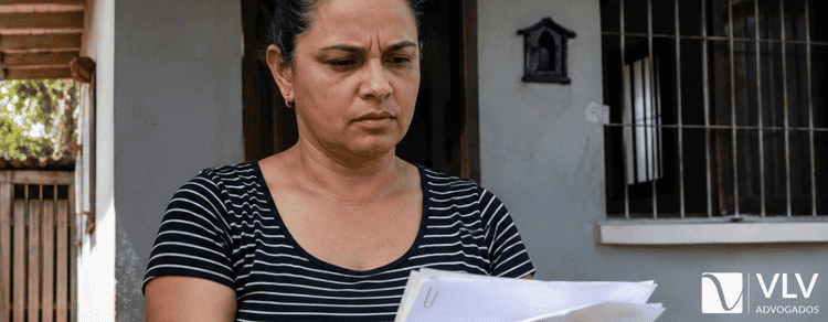 Usucapião: quando você tem direito e quantos anos precisa 1 mulher em frente a sua casa com papéis do imóvel na mão para pedir usucapião